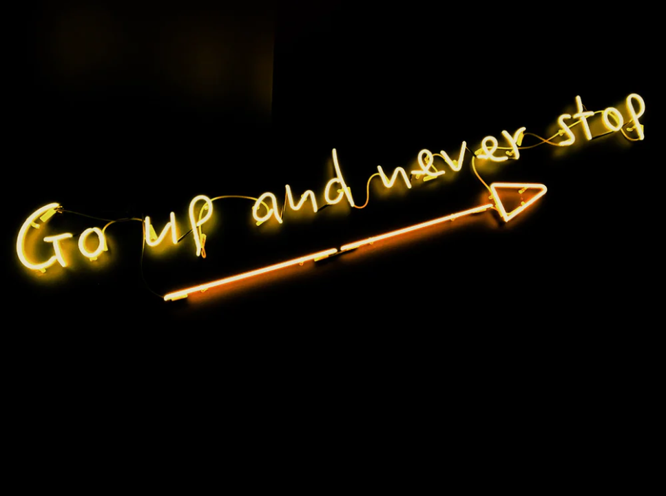 A neon sign reading go up and never stop