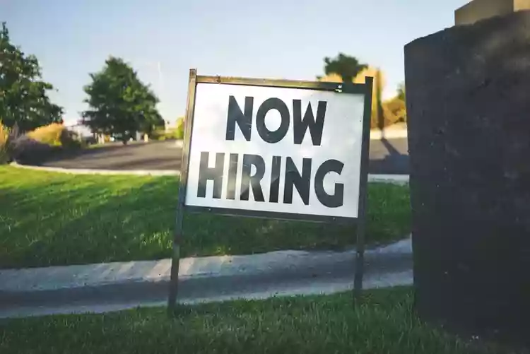 Now Hiring sign in the grass along a road