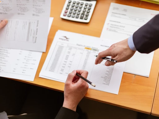 Two people using pens to point at paper on a desk